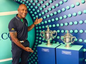 Kevin Ware posing beside championship tennis trophies at a tennis event exhibit.